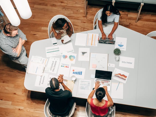 Plusieurs personnes sont assises autour d'une table avec des ordinateurs portatifs et des cahiers déposés dessus.